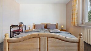 Una cama de madera con cabecera, mesitas de noche, una silla y una ventana con cortinas.