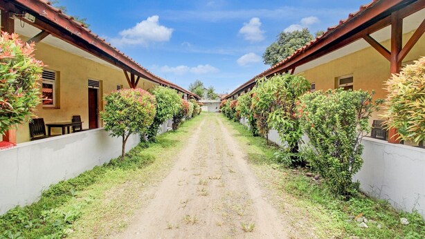 A pathway leading to a building with a red roof and white walls, surrounded by greenery.