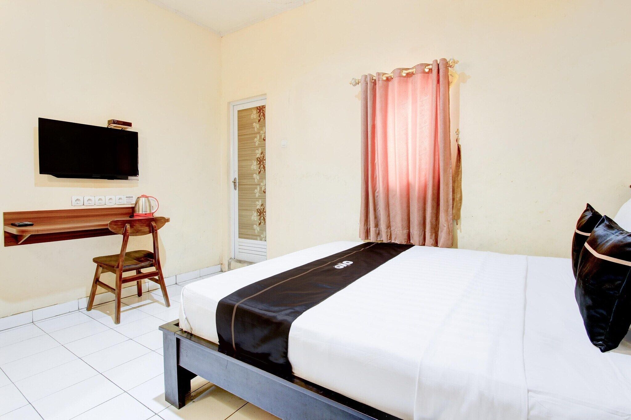 A hotel room with a bed, a desk, a chair, a television, and a window with curtains.
