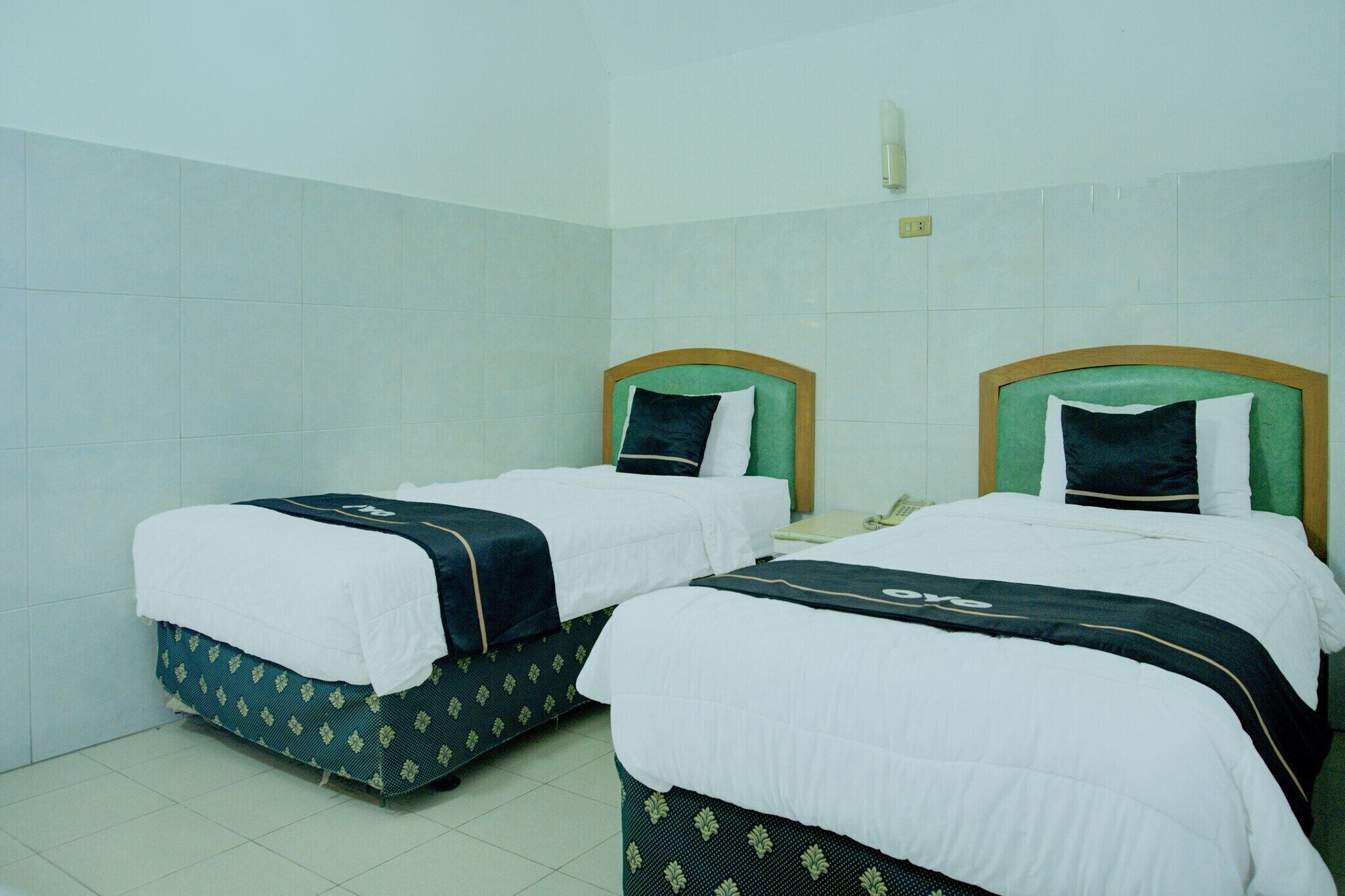 A hotel room with two beds, each with a green headboard, white bedding, and a patterned skirt.