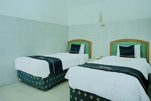 A hotel room with two beds, each with a green headboard, white bedding, and a patterned skirt.