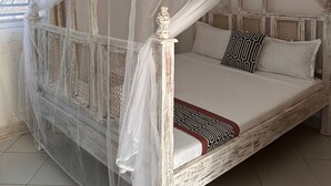 Ein Bett mit Baldachin, weiße Bettwäsche und gemusterte Kissen.