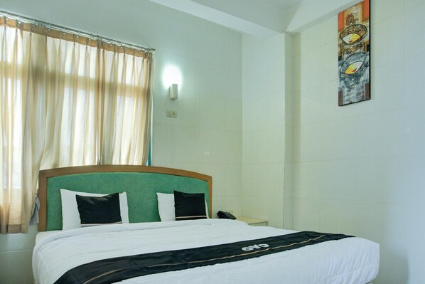 A hotel room with a bed, curtains, a wall-mounted light, and a painting.