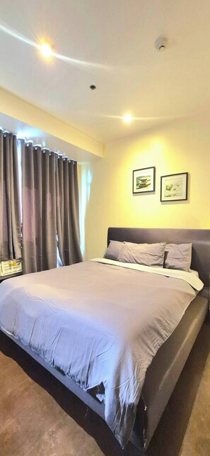 Ein Schlafzimmer mit einem Bett, Vorhängen, einem Kopfteil und zwei gerahmten Bildern an der Wand.