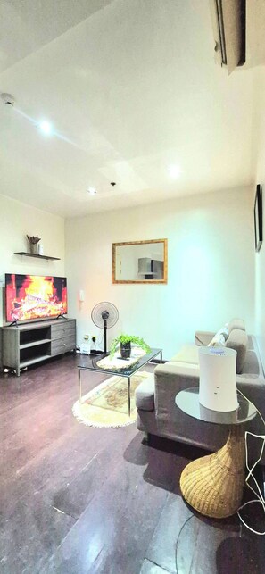 Ein Wohnzimmer mit Flachbildfernseher, Ventilator, Sofa, Couchtisch und einer dekorativen Vase.