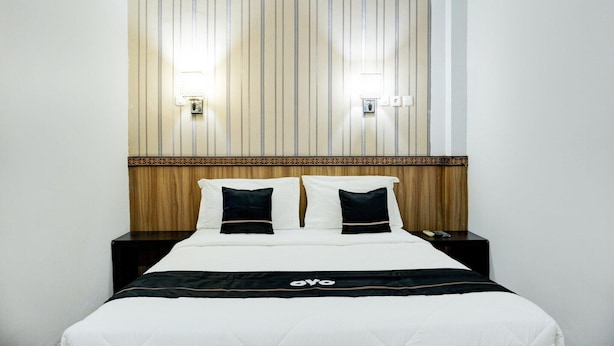 Hotellihuone, jossa on sänky, kaksi yöpöytää, pystysuorilla viivoilla koristeltu sängynpääty ja kaksi seinään kiinnitettyä valaisinta.