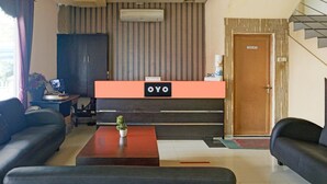 A reception desk with a sign reading 'OYO,' a reception area with a sofa, a small table with a plant, and a staircase to the right.