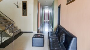 Un vestíbulo de hotel con una escalera, un sofá de cuero negro, un pequeño otoman y un pasillo que conduce a una puerta.