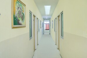Un pasillo con puertas a ambos lados, una lámpara en el techo y un cuadro abstracto enmarcado en la pared izquierda.