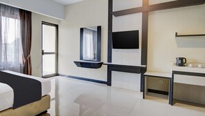 A modern hotel room with a bed, a flat-screen TV, a small desk with a kettle, and a window with curtains.