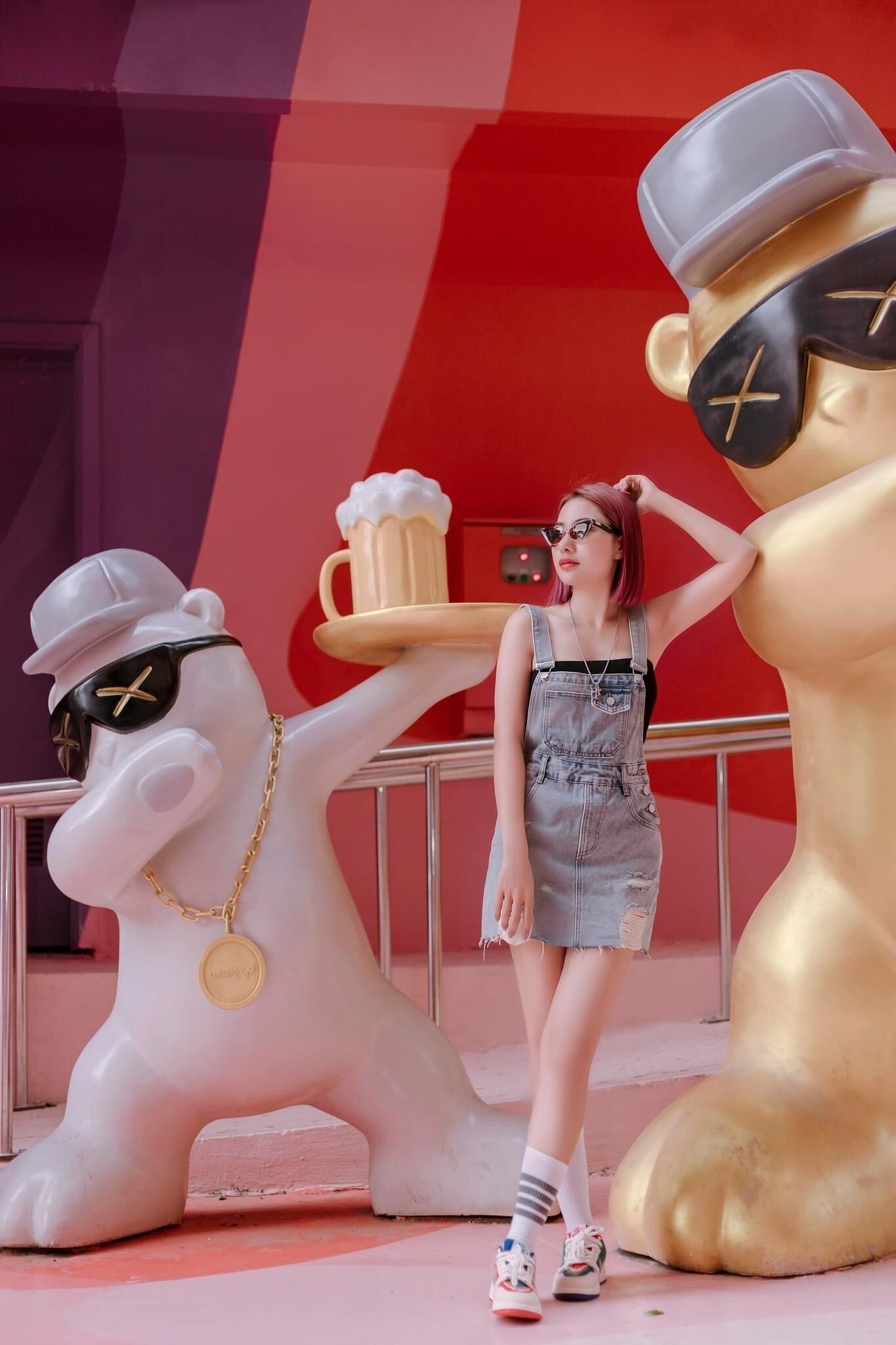 A person standing between two statues, one white and one gold, with a tray of beer.