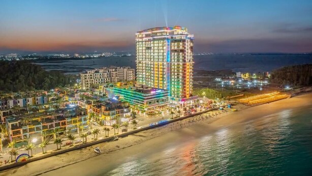 Un hotel moderno de gran altura con varias plantas, ubicación frente a la playa y vistas al mar.