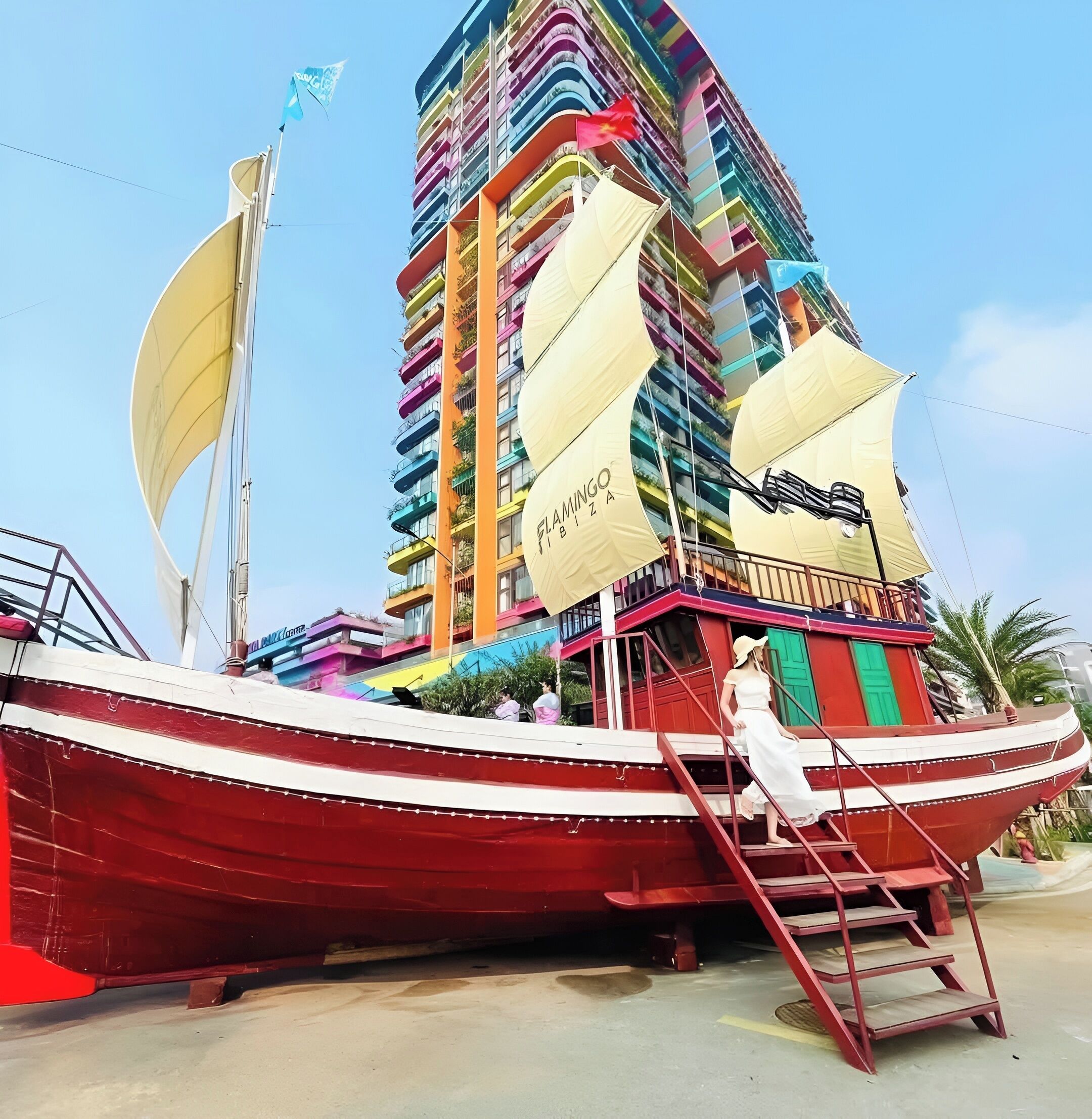 Un edificio grande y colorido con balcones, una bandera y un velero al frente.