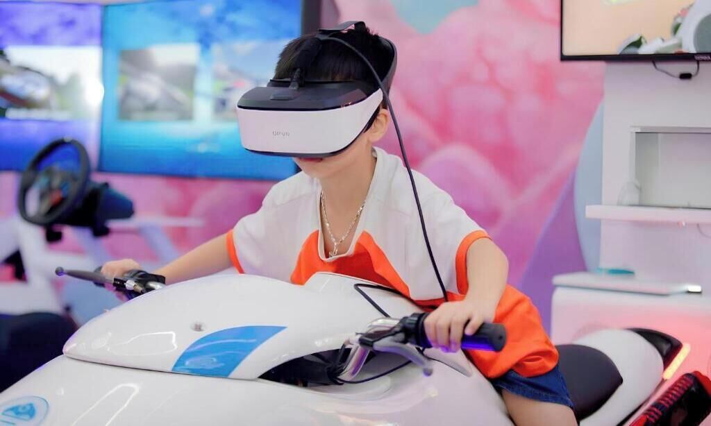 En person som använder ett VR-headset (headset för virtuell verklighet) medan hen sitter på en vit elsparkcykel.
