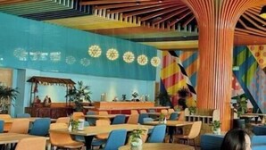 Un restaurante con asientos azules, mesas de madera y un colorido diseño de techo.