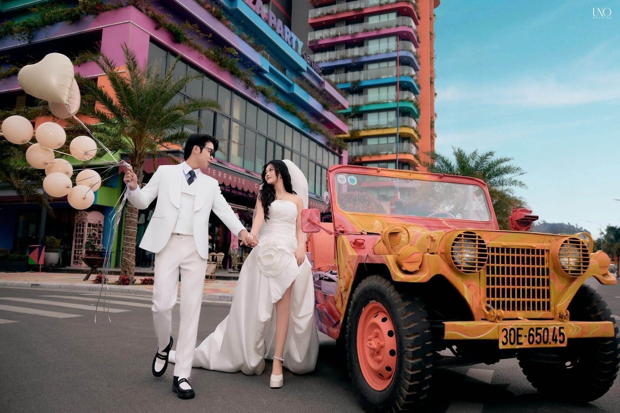 Um casal caminhando perto de um edifício colorido com varandas e um veículo peculiar nas proximidades.