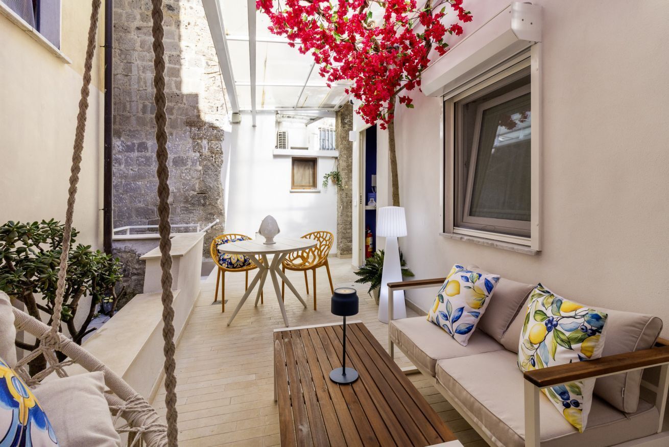 A cozy outdoor seating area with a wooden table, a sofa with patterned cushions, and a dining set.