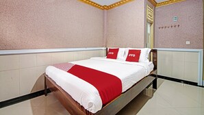 Ein Hotelzimmer mit Bett, einer roten und weißen Tagesdecke und einem an der Wand befestigten Kleiderhaken.