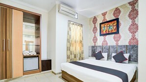 A hotel room with a bed, a wardrobe, a small refrigerator, a shower curtain, and a wall with a patterned design. - Stylish DBL Suite Escape W/ Free WiFi and Parking (Padang)