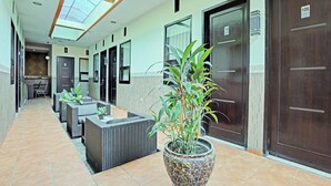 Corredor de hotel com claraboia, portas de madeira escura e um vaso de planta.