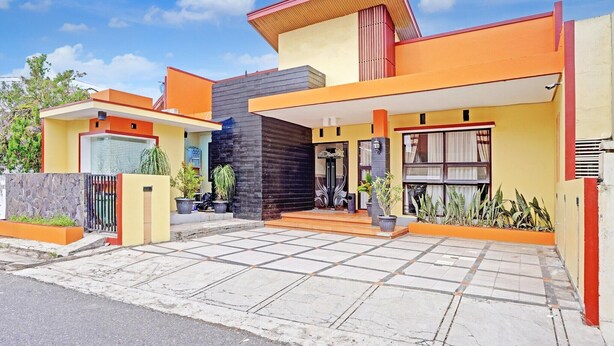 Uma casa moderna de dois andares com telhado plano, varanda frontal espaçosa e portão fechado.