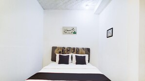 Een net opgemaakt bed met een gestreept hoofdeinde, een lijst met Arabische kalligrafie aan de muur, en een klein fotolijstje.