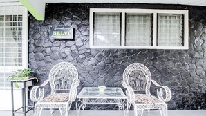 Een stenen muur met een bord waarop 'Guesthouse NELVI' staat, en twee witte metalen stoelen met een glazen tafel ervoor.
