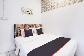 Una cama bien hecha con almohadones estampados y un cabecero, un interruptor de luz en la pared y un adorno decorativo en la pared.