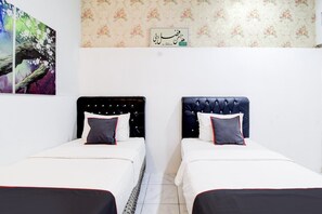 Ein Zimmer mit zwei Betten, jeweils mit Kopfstütze, weißer Bettwäsche und Kissen. An den Wänden befindet sich floraler Wandteppich und ein gerahmtes Schild.