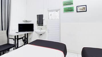 Ein Hotelzimmer mit Bett, Schreibtisch inklusive Computer, Waschbecken und zwei gerahmten Bildern an der Wand.