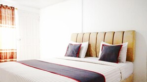 A bed with a striped bedspread and pillows, a wooden headboard, and a white door with a curtain. - Luxury Deluxe Double Retreat with Parking Access (Padang)