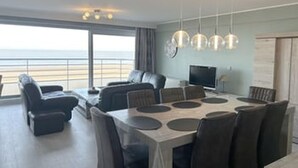 Una sala de estar moderna con un ventanal grande, un comedor con mesa y sillas, y un televisor.