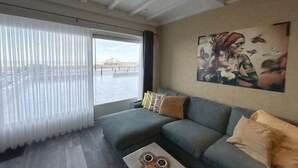 Ett modernt vardagsrum med en soffa, ett soffbord och ett stort fönster med tunna, genomskinliga gardiner.