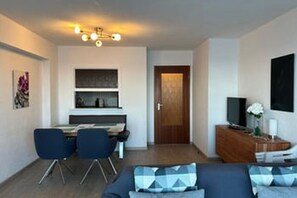 Ein kompakter Wohnbereich mit Essplatz, einer Couch mit Kissen, einem Fernseher und einem Holzschrank.