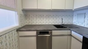Cuina amb armaris blancs, rentaplats d'acer inoxidable i un mosaic decoratiu a la paret.
