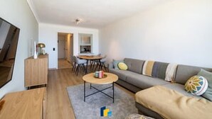 Uma sala de estar moderna com um sofá, mesa de centro e televisão. Há também uma área de jantar com mesa e cadeiras.