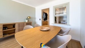 Quarto moderno com mesa de jantar de madeira, cadeiras brancas, guarda-roupa embutido e janela com persianas.