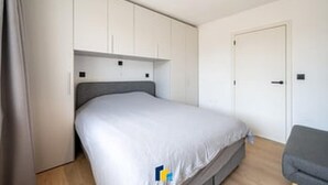 Quarto com cama, guarda-roupa, porta e uma cadeira cinzenta.