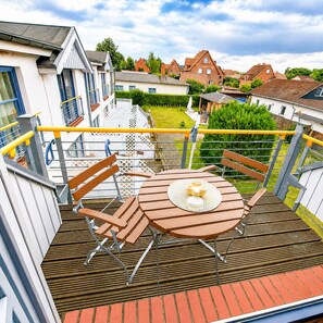 A balcony with a round table and chairs, a yellow railing, and a view of houses in the background. - Haus Meeresrauschen (Rerik)