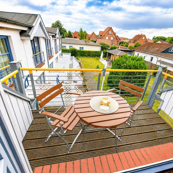 A balcony with a round table and chairs, a yellow railing, and a view of houses in the background.