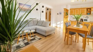 Una sala moderna con un sofá gris, una mesa de comedor con sillas, y una zona de cocina con armarios de madera y un microondas.