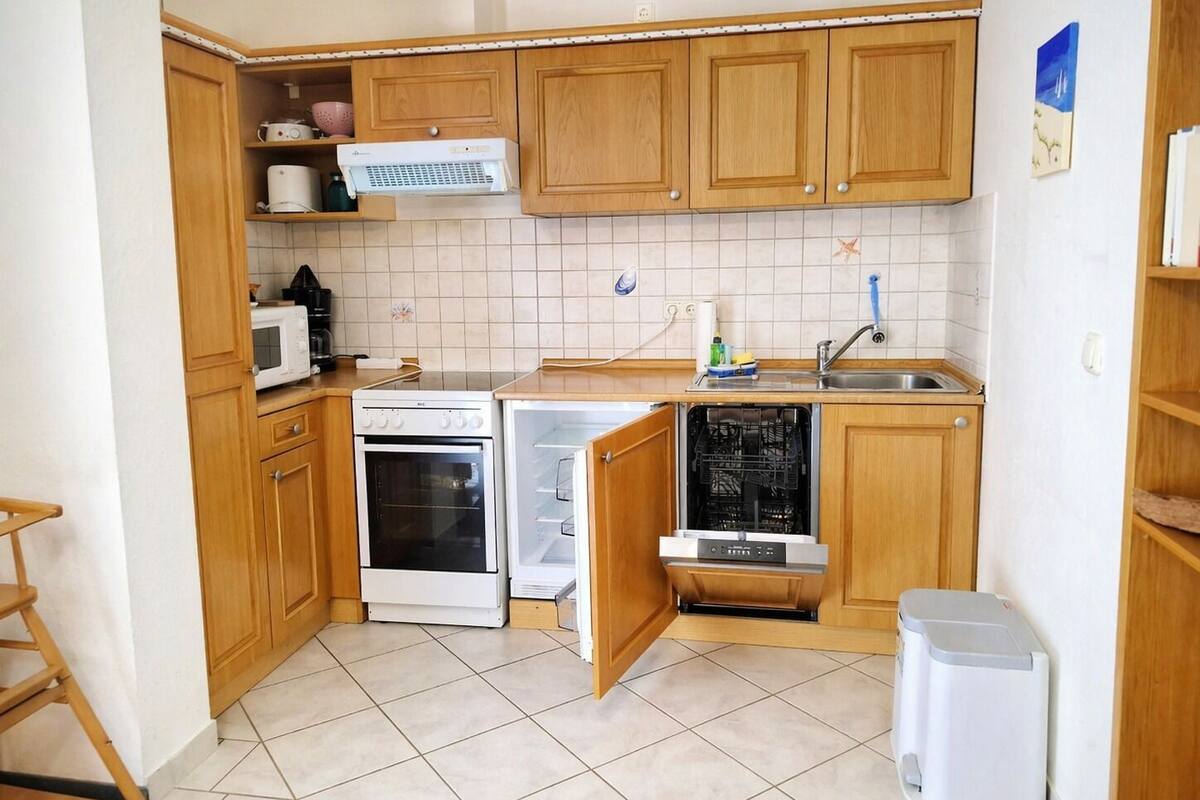 A compact kitchen with wooden cabinets, a microwave, an oven, a dishwasher, and a small trash bin.