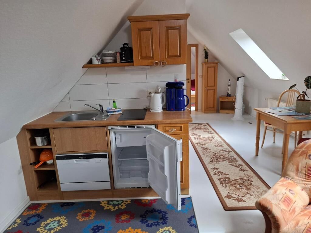 A compact kitchen with a dishwasher, a coffee maker, and a small refrigerator. There is a wooden cabinet above the sink and a window providing natural light.
