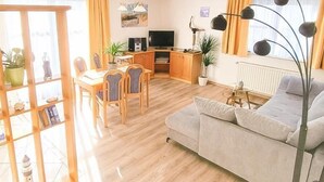 Una sala de estar con un sofá, una mesa de comedor con sillas, un televisor y una planta.