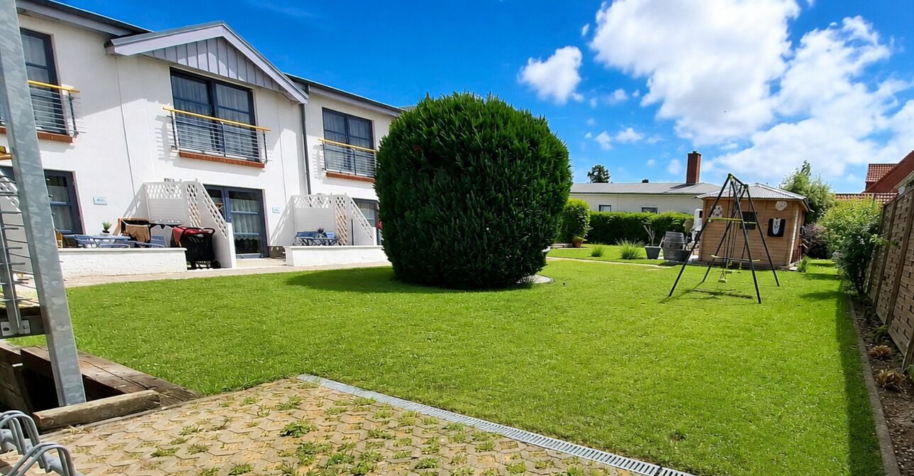 A residential property with a well-maintained lawn, a large coniferous tree, a swing set, and a small shed.