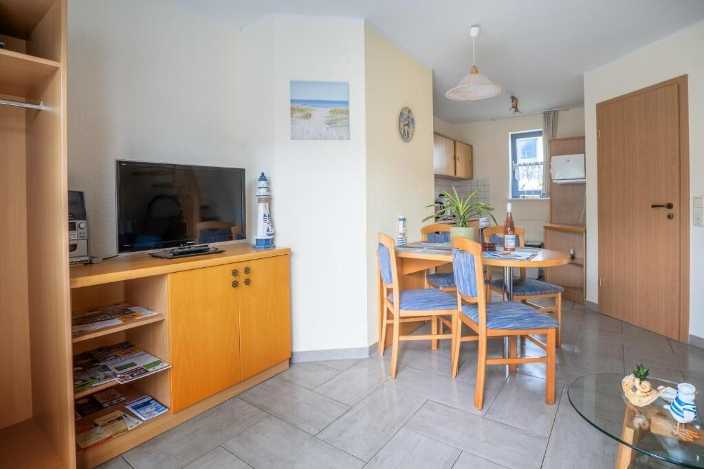 A compact kitchen with a dining area, wooden cabinets, a television, and a small table with chairs.