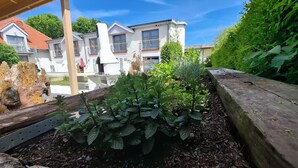 Un jardín con plantas, un banco de madera y un edificio blanco con balcones.