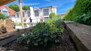 A garden area with plants, a wooden bench, and a white building with balconies.