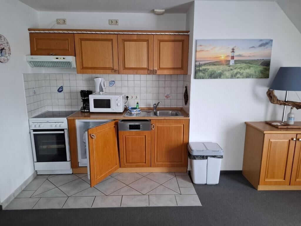 Cocina compacta con armarios de madera, microondas, estufa y lavamanos.