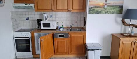 Cocina compacta con armarios de madera, microondas, estufa y lavamanos.
